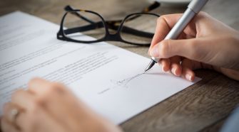 Closeup shot of a woman signing a form. She's writing on a financial contract. Shallow depth of field with focus on tip of the pen.